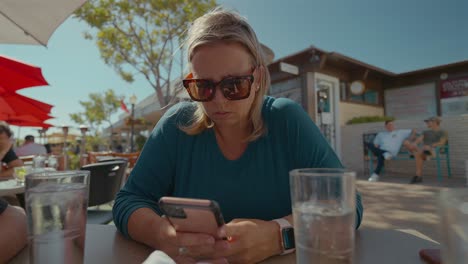 Mujer-Caucásica-Jugando-En-El-Teléfono-Celular-Mientras-Cena-Al-Aire-Libre