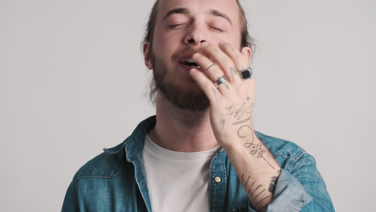 un joven caucásico bostezando ante la cámara.