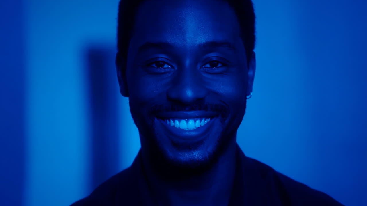 Close-up portrait of a smiling man under blue light