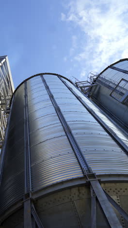 modern granary under blue sky. large aluminum containers for storing grains. exterior of grain elevators. close-up. view from below. vertical video