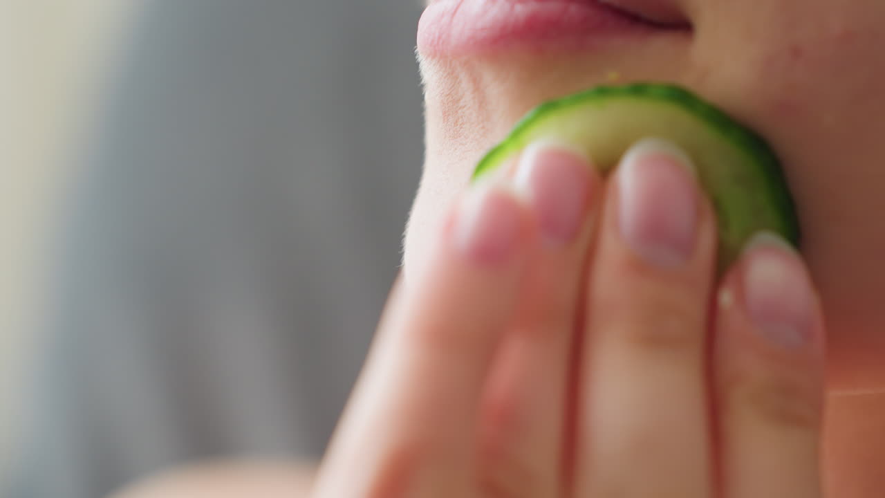 Close-up of woman gently massaging cucumber slice on cheek during skincare routine, highlighting smooth skin texture, hydration, and calming beauty ritual focused on freshness, glow