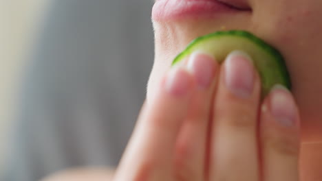 close-up of woman gently massaging cucumber slice on cheek during skincare routine, highlighting smooth skin texture, hydration, and calming beauty ritual focused on freshness, glow