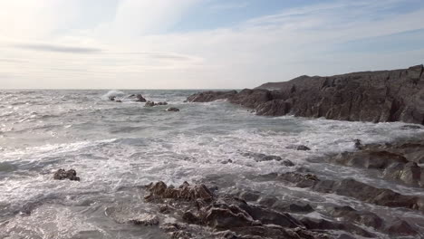 right to left pan of waves crashing against a rocky cove on a summer’s evening