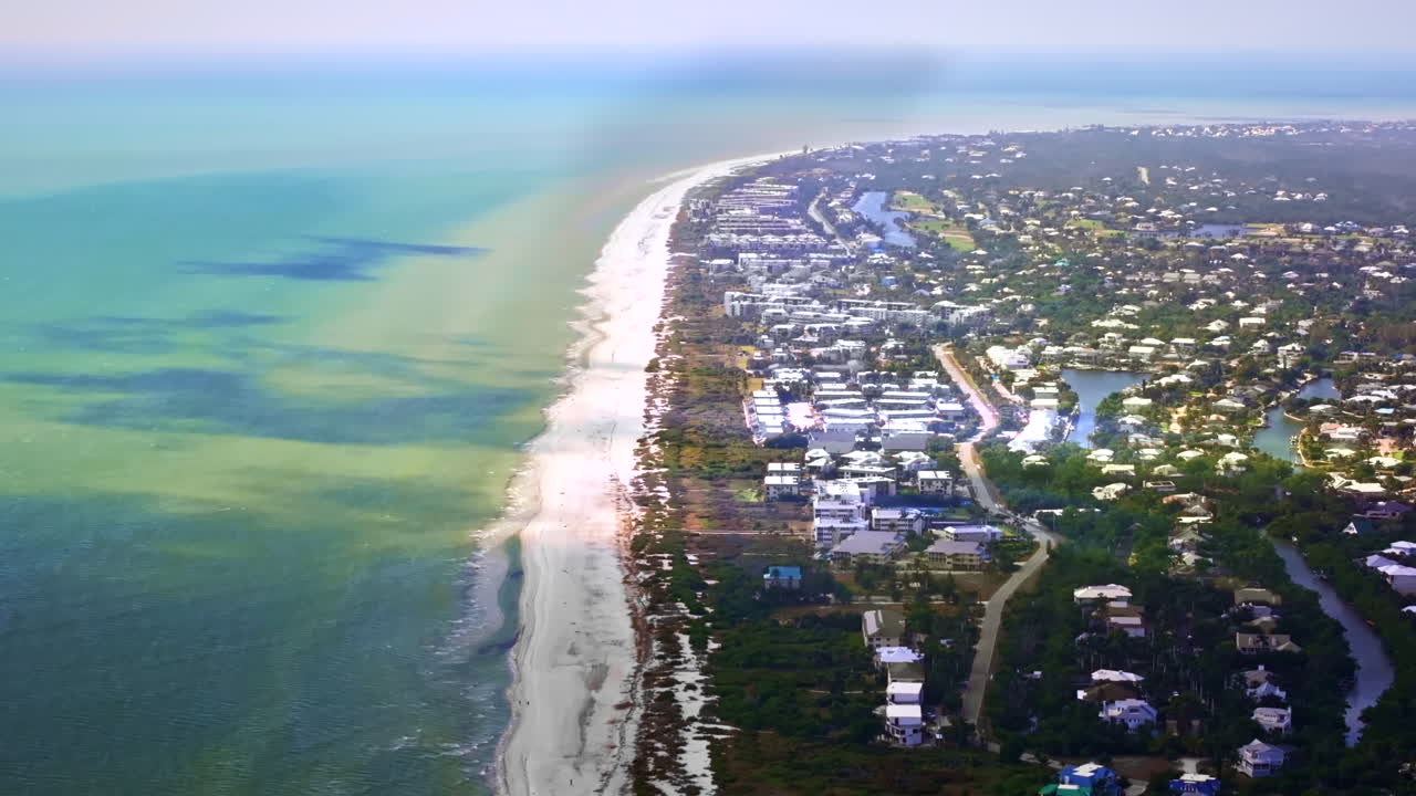 Uma tomada aérea cinematográfica de drone de 70mm recuando ao longo da costa da Ilha Sanibel, Flórida, uma costa intocada perto de Fort Myers, e lar do histórico Farol da Ilha Sanibel