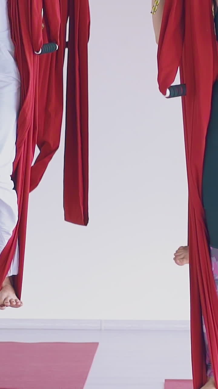 concentrated pretty women group synchronously stands up holding long oriental fly yoga hammocks slow motion