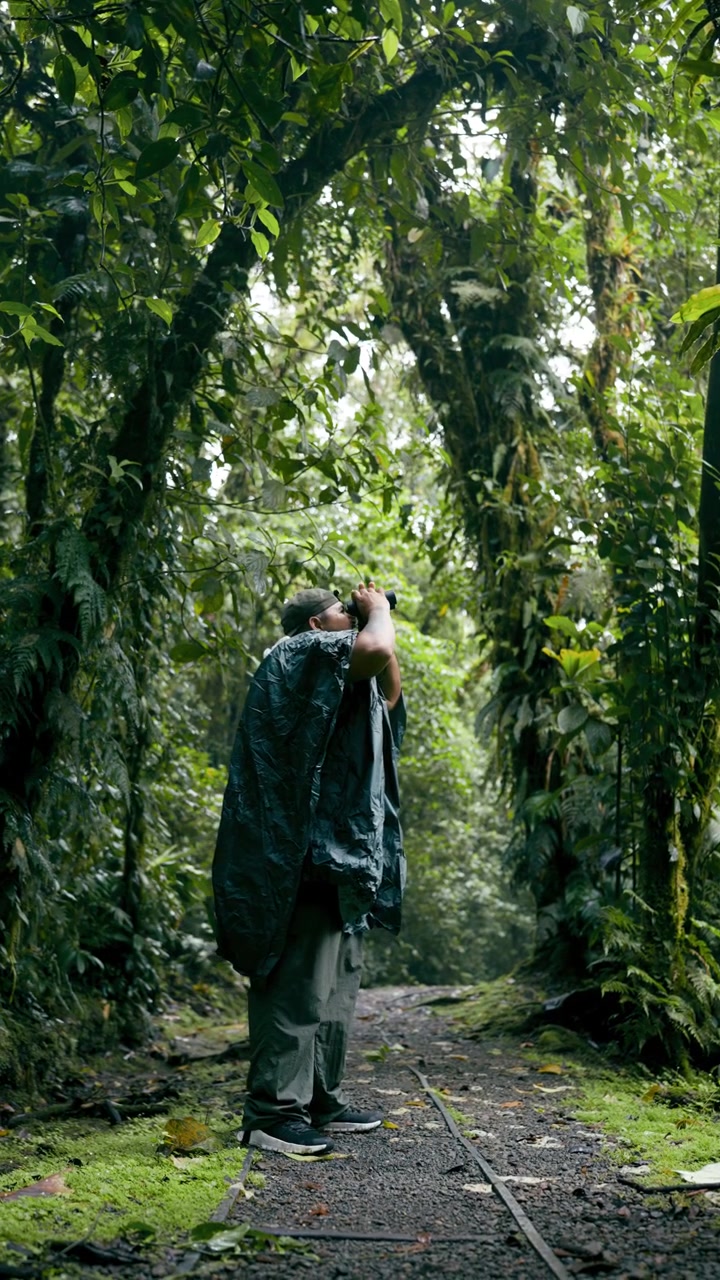 Uomo con poncho antipioggia che fa birdwatching in rigogliosa foresta pluviale tropicale