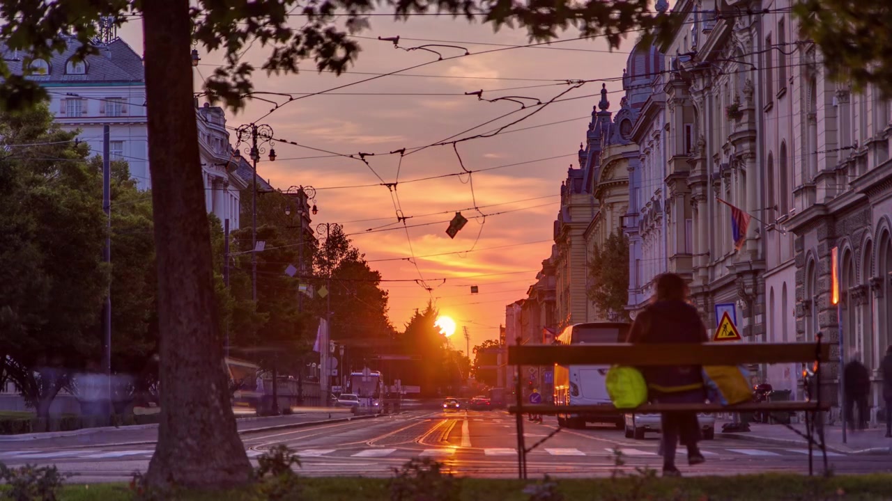 Straße mit Sonnenuntergang in der kroatischen Hauptstadt Zagreb. Menschen sitzen auf einer Bank nahe einem Baum.