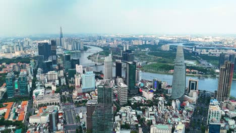 a wide zoom-out drone shot of the ho chi minh city skyline with the saigon river, modern skyscrapers, and landmark 81 under a hazy blue sky, vietnam.