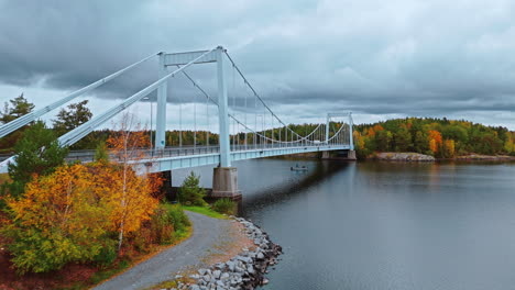 approaching a suspension bridge crossing a lake surrounded by an autumn forest with green, yellow, brown and red trees in valkeakoski, finland