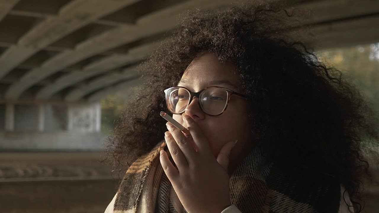 Donna con capelli ricci e pelle scura che fuma una sigaretta nel freddo clima autunnale