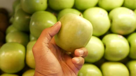 hand holding a green apple in front of a pile of apples