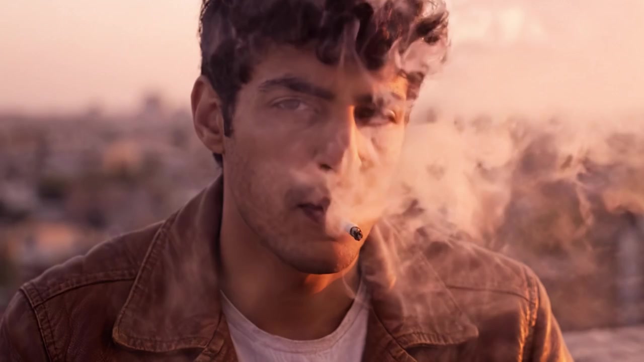 Un uomo pensieroso che guarda in lontananza mentre fuma, catturato in una scena al tramonto che riflette introspezione e vita urbana.