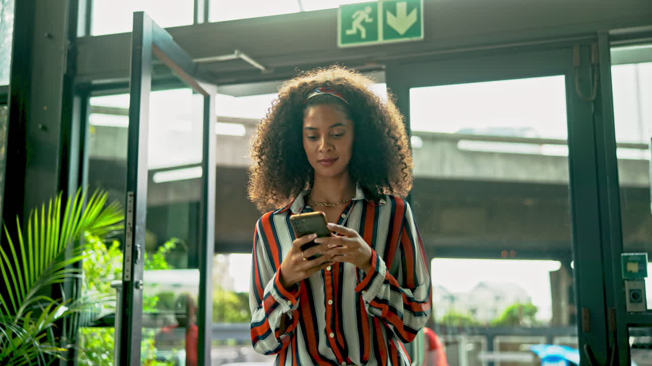A woman with curly hair using a smartphone indoors