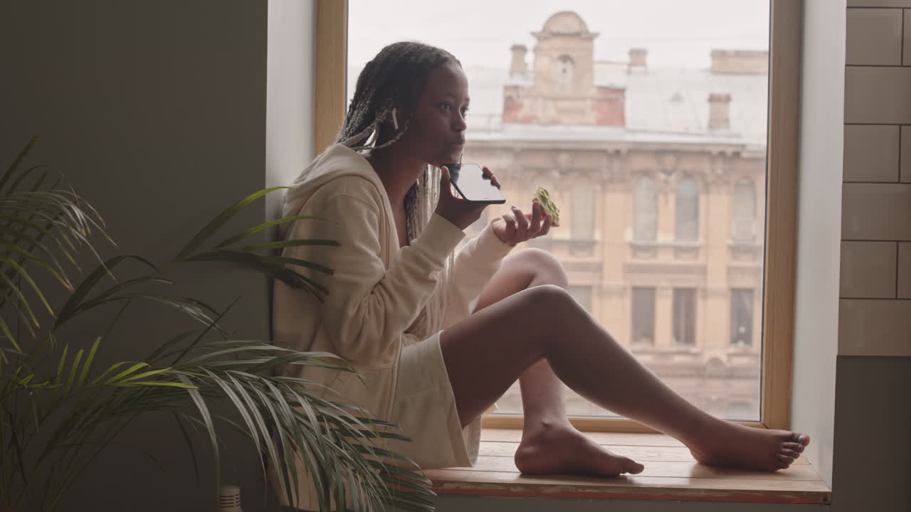 Donna afroamericana che chatta al cellulare sul davanzale