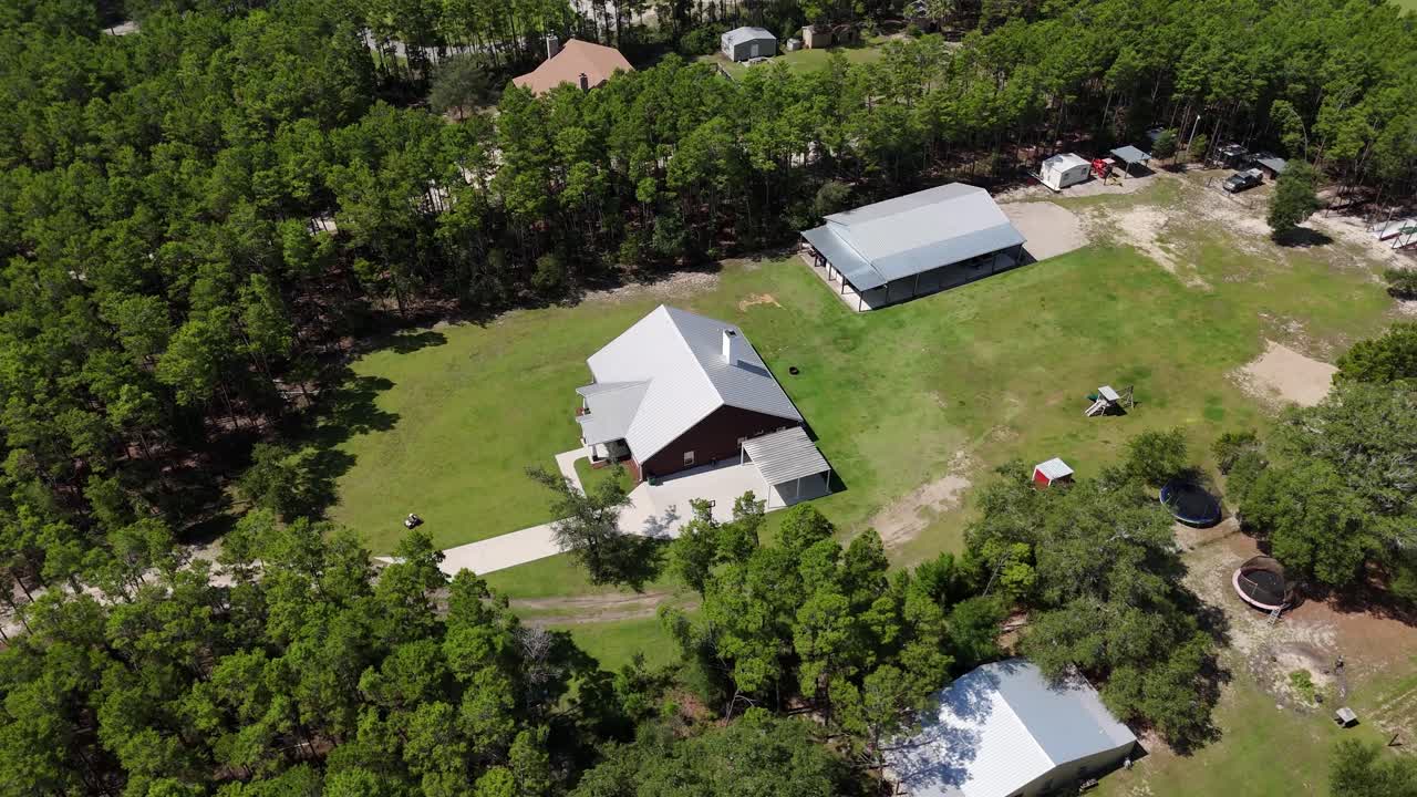 Dynamic aerial fly around rural farm estate buildings surrounded by dense green forest, Panama City Beach, Florida, USA