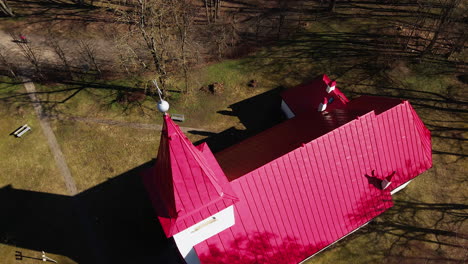 vista aérea de la iglesia luterana lielvarde en la orilla del río daugava, iglesia blanca con techo rojo, árboles sin hojas, día soleado de primavera, amplio tiro de ojo de pájaro avanzando