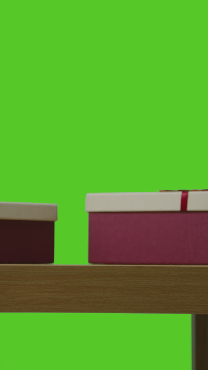 남자 가 선물 로 포장 된 상자 에 있는 선물 을 집어 들고 내려 놓는 수직 비디오 - 테이블 에서 녹색 스크린 에 맞춰 찍은 영상 1