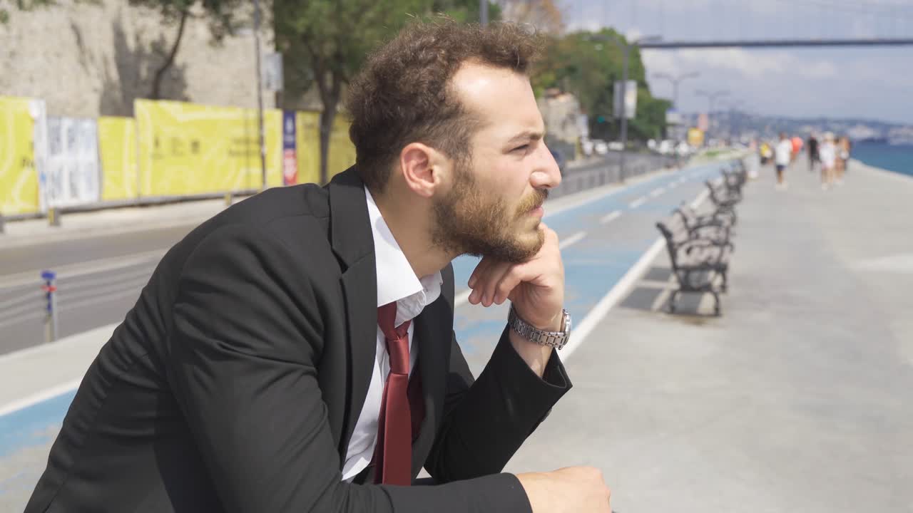 Uomo d'affari annoiato seduto su una panchina in riva al mare in città