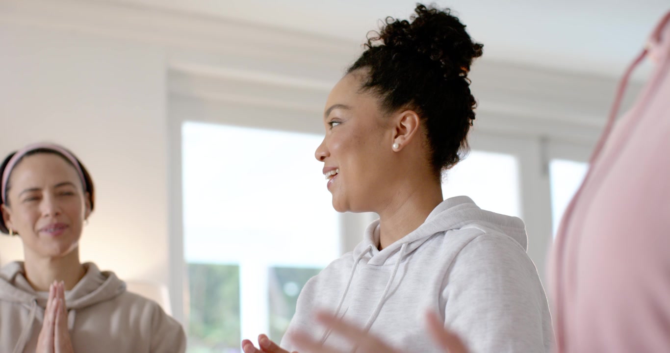 Diverse women following gray woman closing eyes, breathing for calm in hoodies by window
