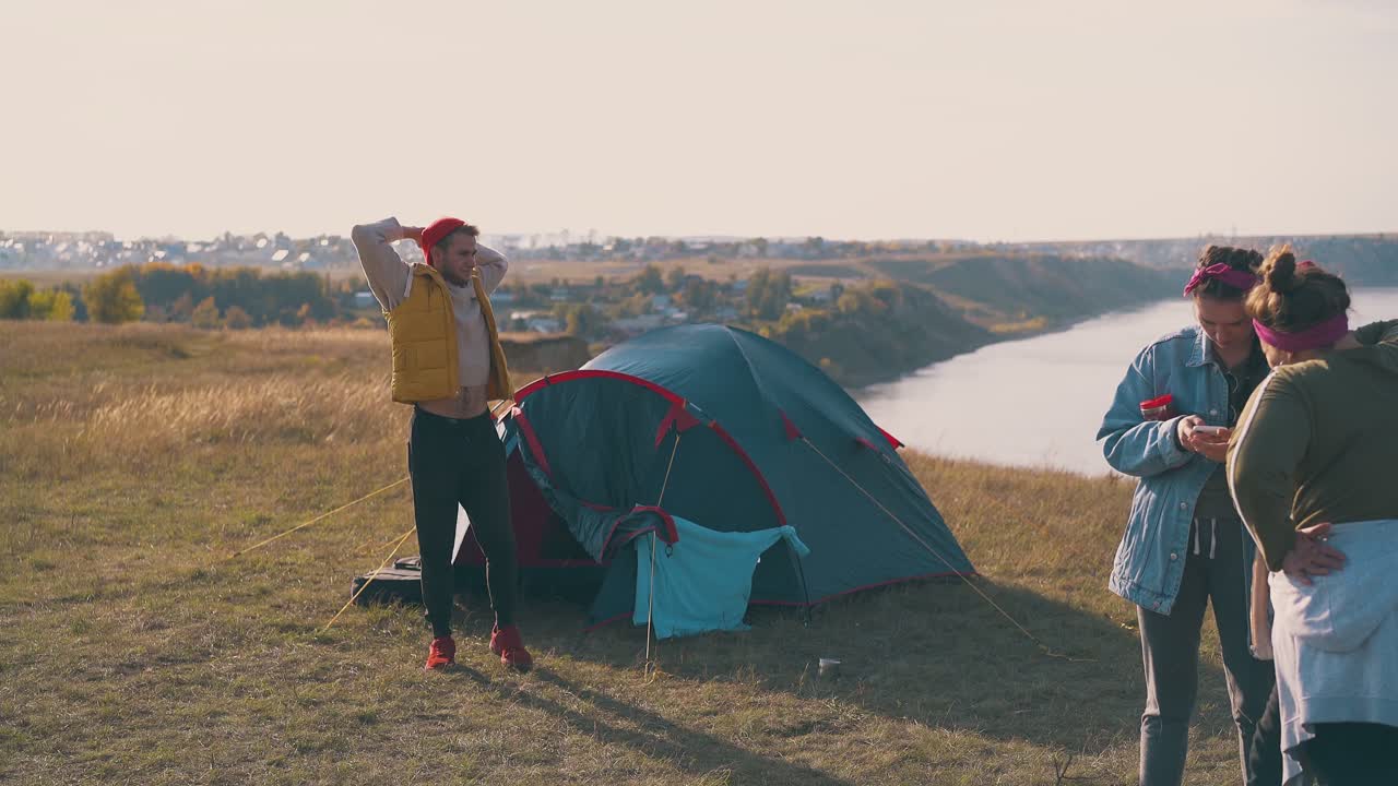 남자는 텐트 밖으로 나가고 여자들은 아침에 은행에 캠프에 있습니다.