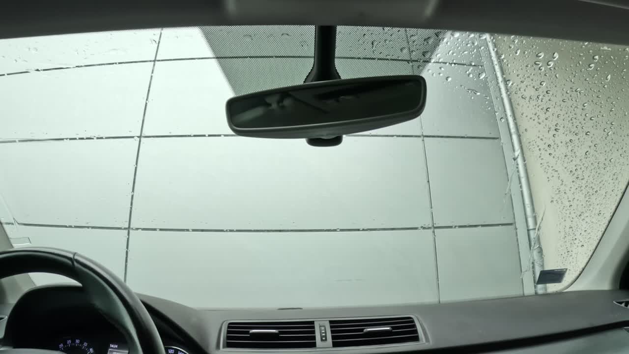 Rain slides down a parked car’s windshield as wipers move slowly, creating a calm, reflective mood from inside the quiet cabin—soft motion, gentle ambience, slow-life atmosphere