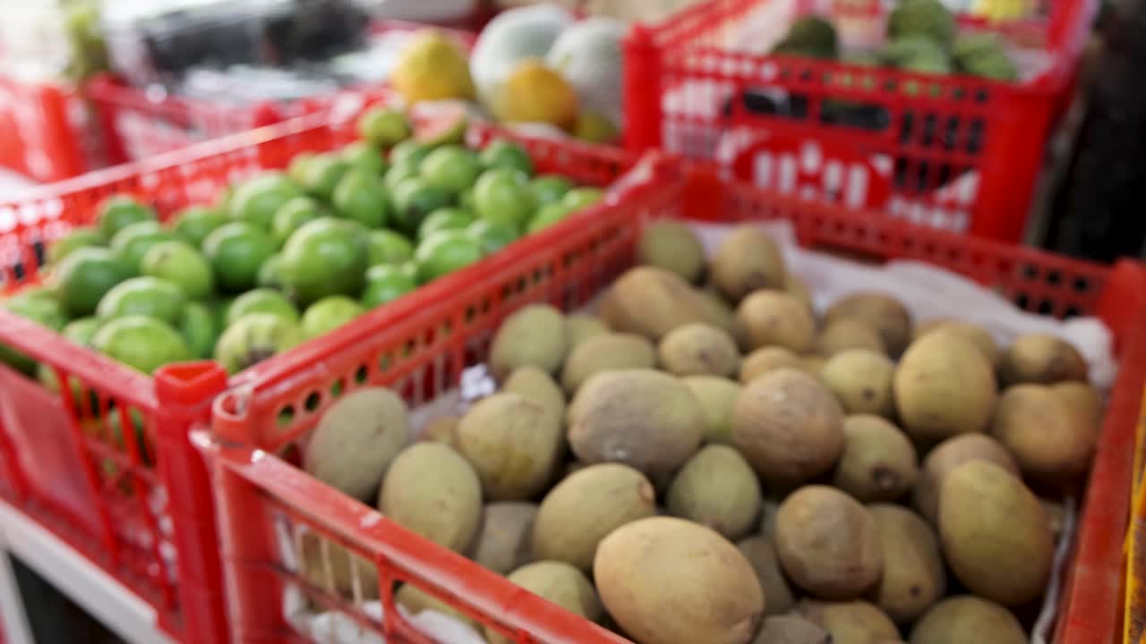 Camera pans across baskets of pomegranates, guavas, and sapodillas at an indoor produce market in Singapore, with natural lighting and shallow depth of field
