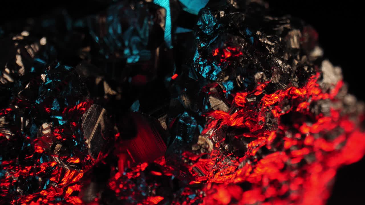 Ripresa dettagliata e vibrante di cristallo di pirite dorato che risplende su sfondo scuro, illuminato da luci rosse e blu