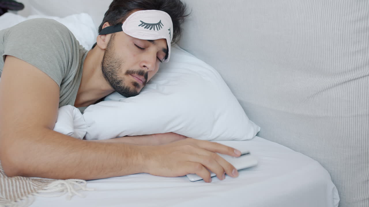 Man Sleeping in Bed with Sleep Mask and Phone