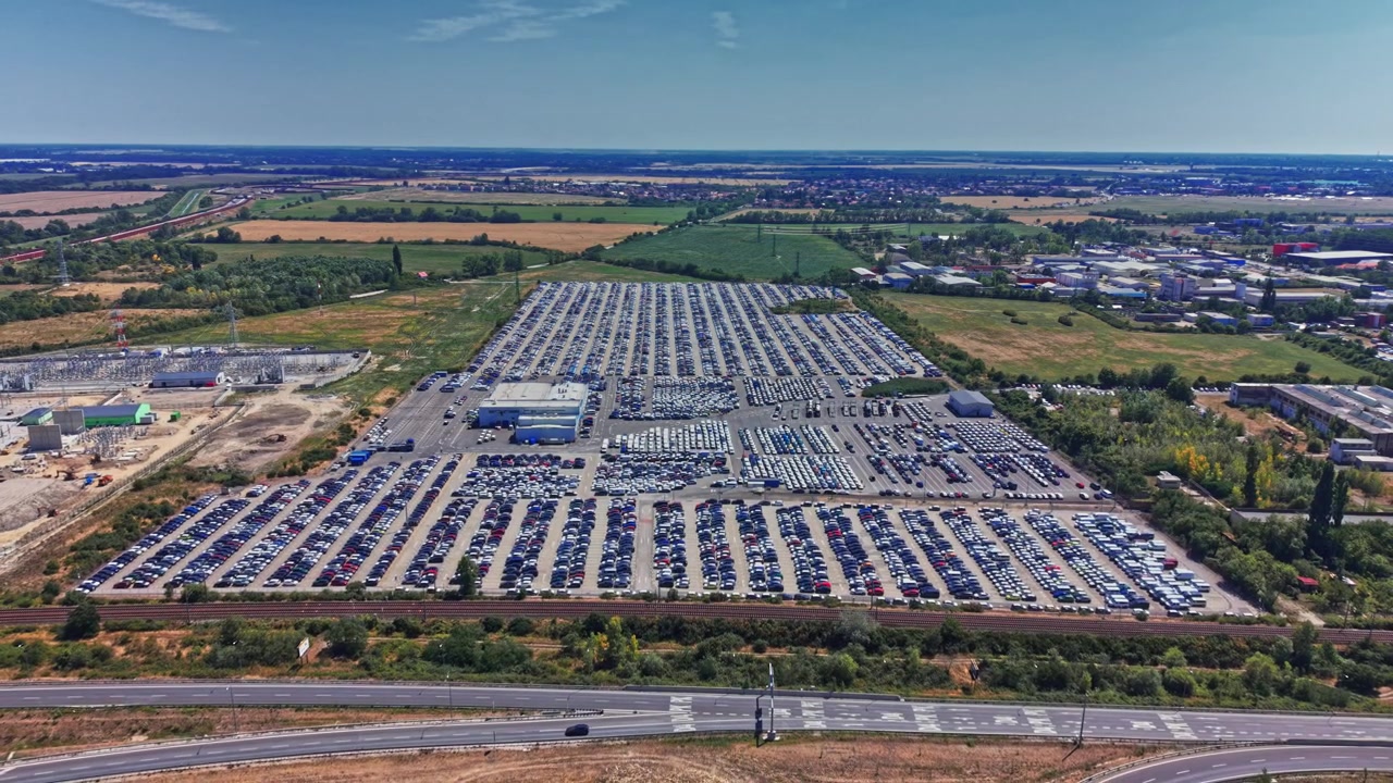 Parking z wieloma samochodami i zielonymi roślinami, widoczny z góry.