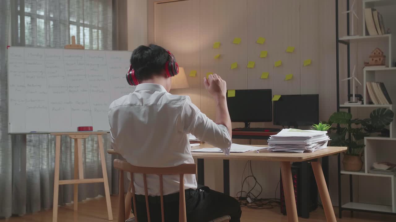 사무실에서 문서를 처리 한 후 춤추기 전에 음악을 듣기 위해 헤드폰을 착용 한 아시아 남자의 뒷면