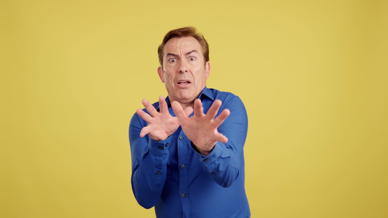 Man expressing fear or aversion with hands outstretched on yellow background