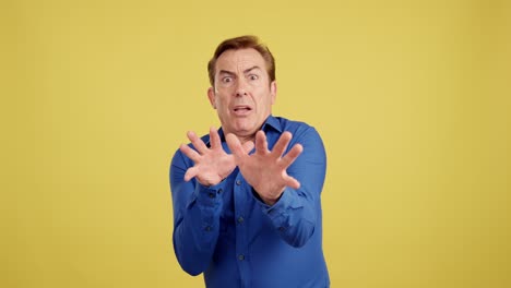 man expressing fear or aversion with hands outstretched on yellow background