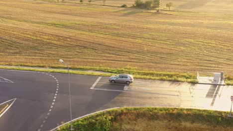 Coche-Plateado-Moviéndose-Por-La-Nueva-Carretera-Asfaltada-Al-Atardecer:-Disparo-Aéreo-De-Drones