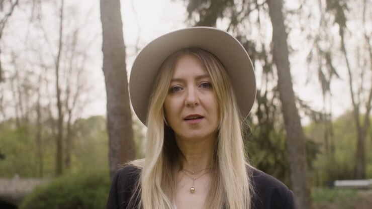 portrait d'une femme blonde avec un chapeau debout dans le parc et regardant la caméra