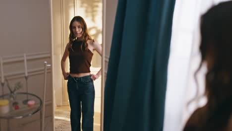 woman reflection trying clothes large jeans at home. smiling girl getting ready