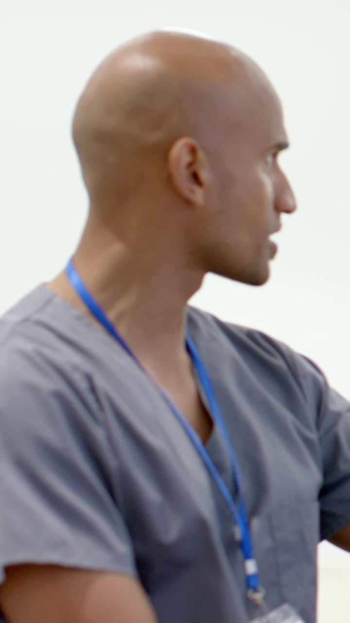 Vertical video: Speaking clinician turning to monitor during consult in grey scrubs, ID lanyard