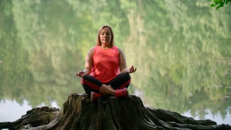 a woman in sportswear practicing breathing yoga on a log over the forest lake