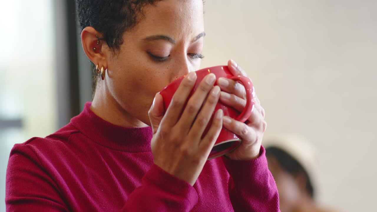 Kvinde i rullekrave indånder aroma fra stort rødt keramikkrus og nipper for at nyde smagen på en café
