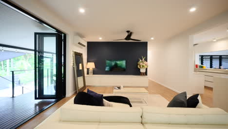 modern living room with pine floorboards, bi-fold doors leading out to balcony, grey feature wall, modern dc fans, and white decor