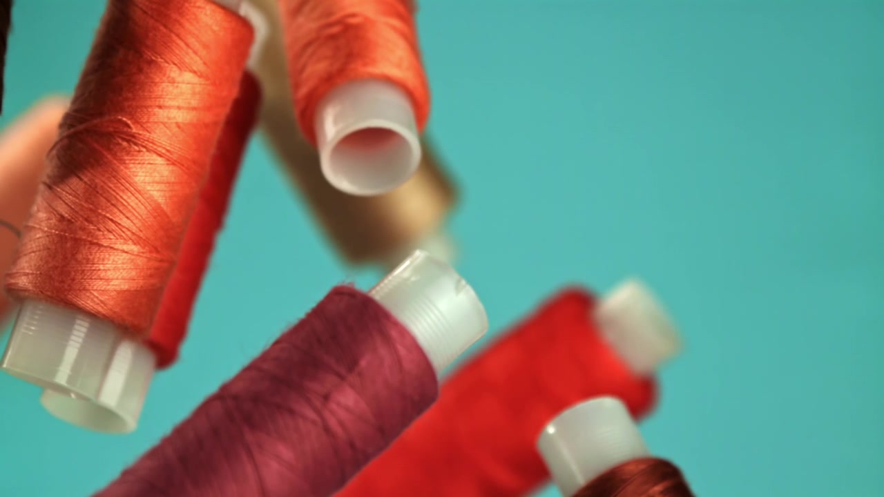 Colorful Thread Spools Falling in Slow Motion Against Teal Background