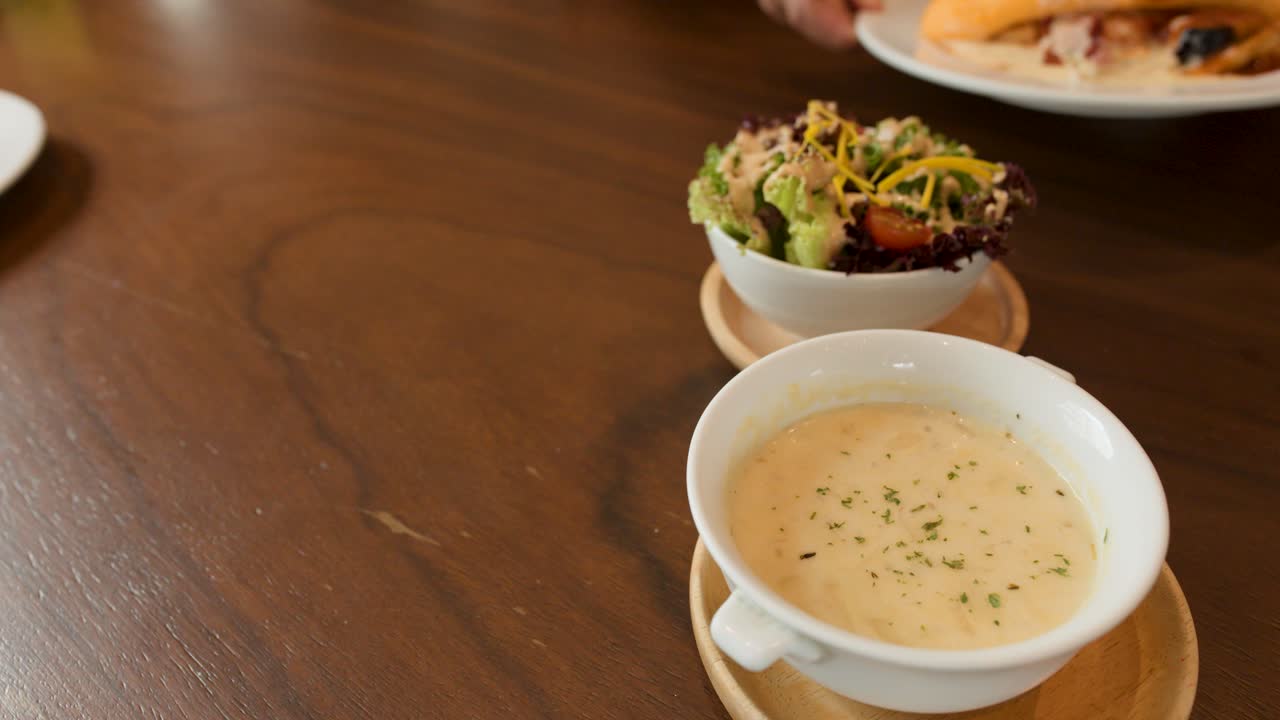 Hand places Japanese omelette rice, salad, and soup on wooden table under warm indoor lighting