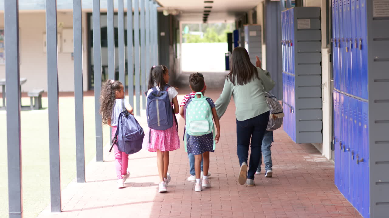 Walking in school hallway, teacher guiding group of students with backpacks