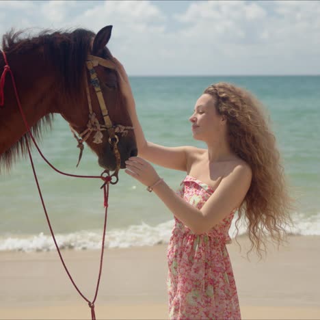 Long-haired-woman-stroking-brown-horse-in-face-on-seaside