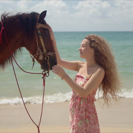 long haired woman stroking brown horse in face on seaside