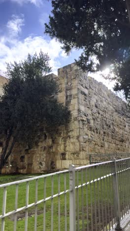 a wall made of stone blocks with a building in the background. jerusalem old city wall.