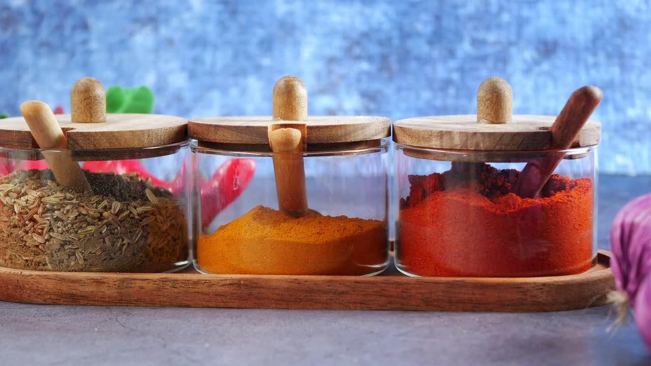 Assortimento di spezie colorate in barattoli di vetro su un vassoio di legno.