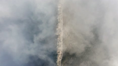 rocky cliff is visible between thick fog in mountains, top down aerial