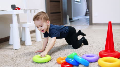 cute baby boy plays on the carpet in his room. cheerful kid plays with the parts of toy pyramid.