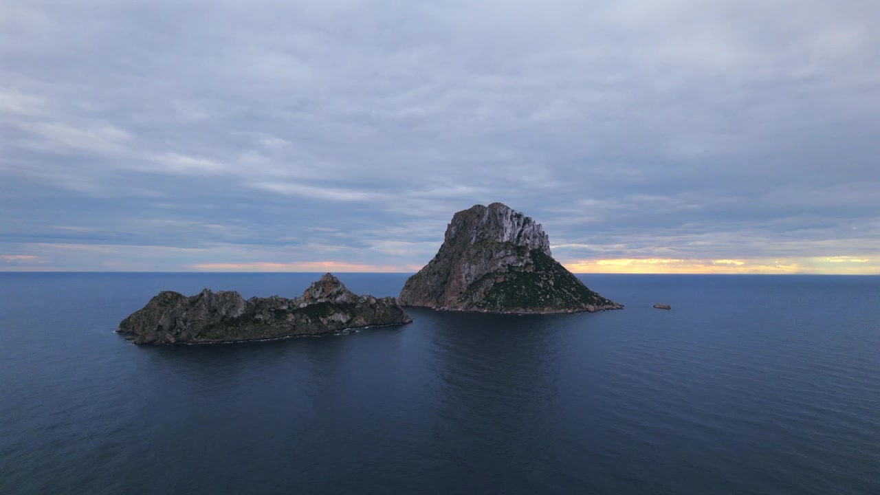 Ripresa aerea in 4K con drone di Es Vedrà al tramonto, Ibiza, Spagna. L'iconica isola rocciosa emerge dal Mar Mediterraneo mentre una calda luce dorata illumina la costa e le acque circostanti