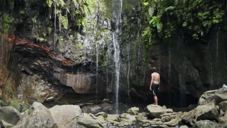 Panning-up-to-man-watching-Levada-das-25-Fontes-run-down-rocks,-Madeira-PT